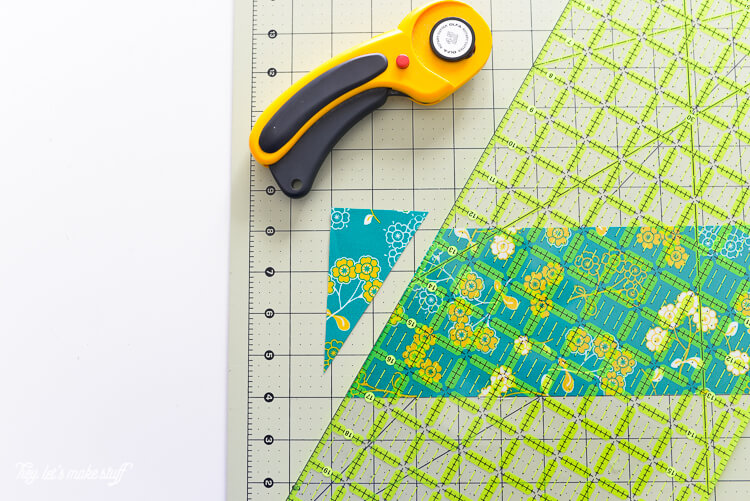 A fabric cutter, an Omnigrip ruler, and a piece of material cut into one triangle all sitting on a fabric mat