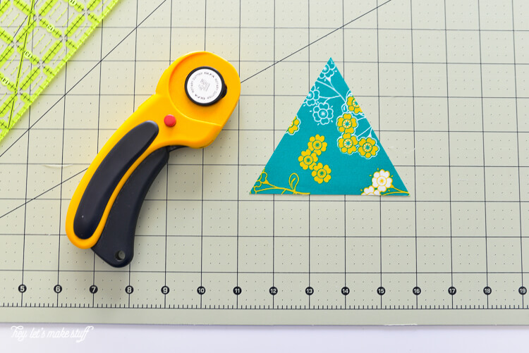 A fabric cutter, an Omnigrip ruler, and a piece of material cut into a triangle all sitting on a fabric mat