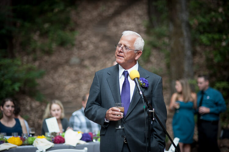 An older gentleman holding a glass of champagne and standing next to a microphone