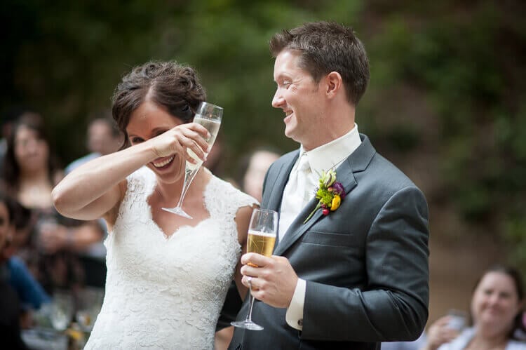 A bride and a groom laughing and holding a glass of champagne