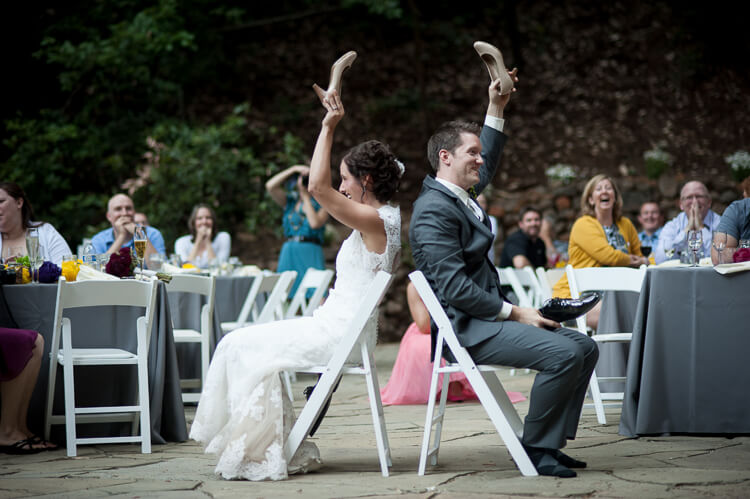 A bride and a groom sitting back-to-back and each holding one of each other\'s shoes