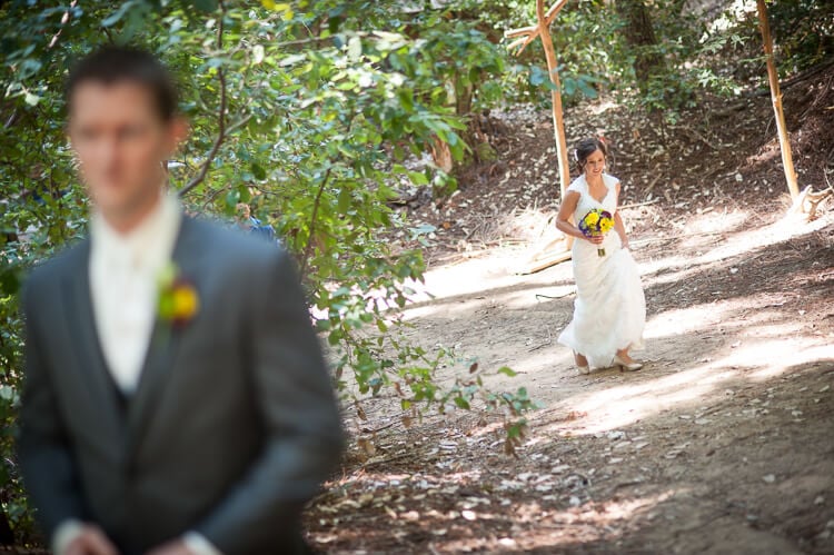 A man standing in the foreground and a bride walking up a trail 