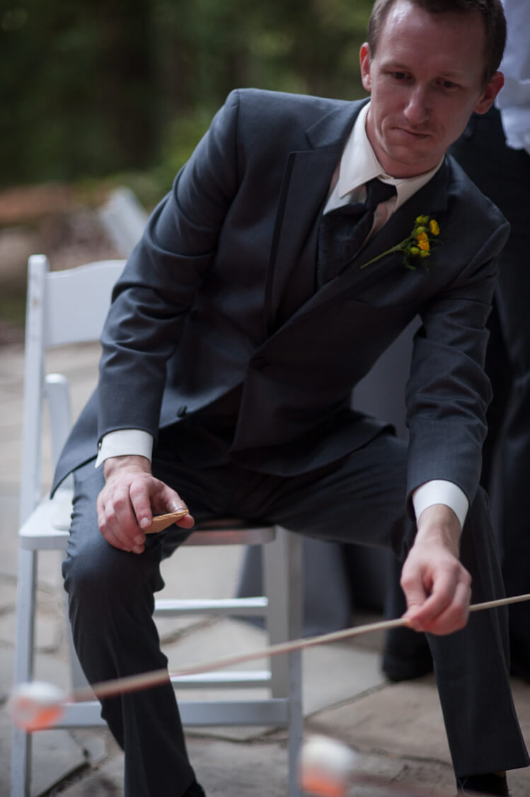 A man in a suit and tie sitting on a chair roasting a marshmallow