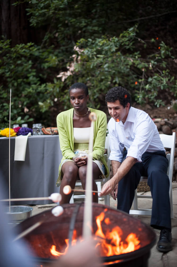 A man and a woman sitting in front of a grill roasting marshmallows