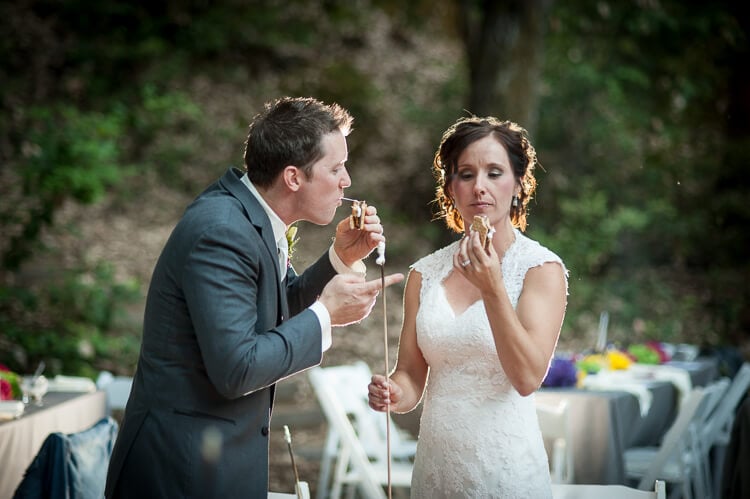 A bride and groom standing and eating a s\'more