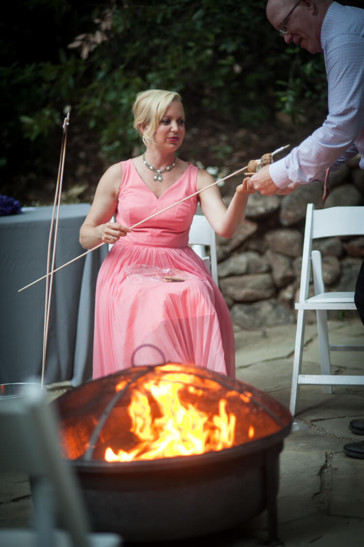 A woman sitting in front of a grill a man helping her make a s\'more