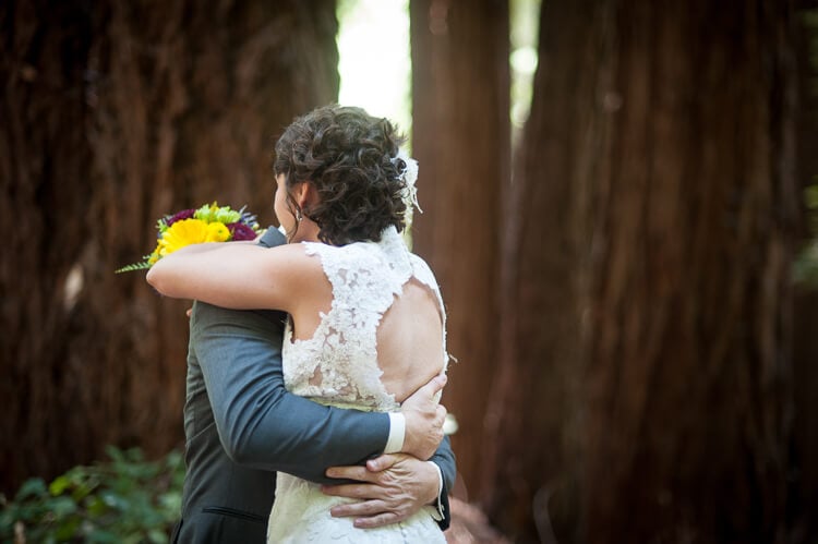 A bride and a groom standing among trees and hugging each other
