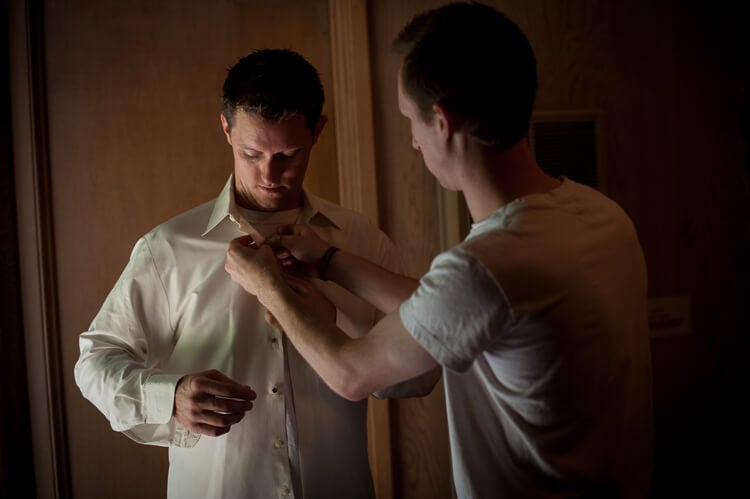 A man helping another man button up his shirt