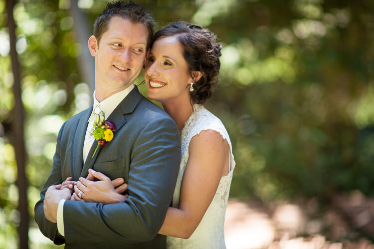 A bride and a groom standing among trees and hugging each other