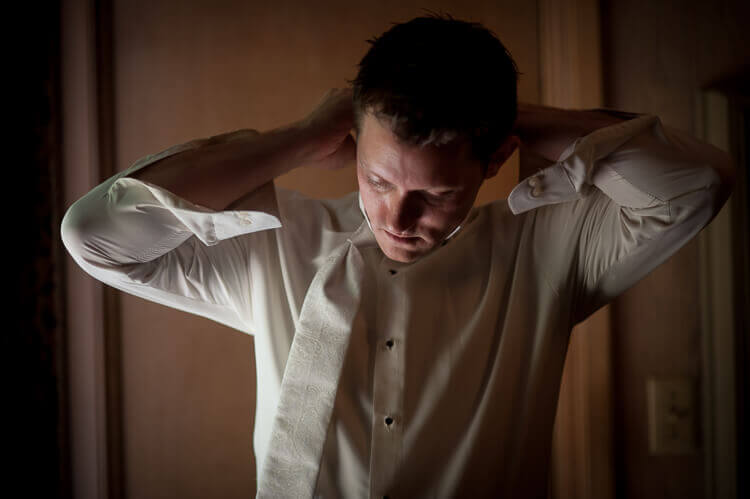 A man standing in a room putting on a tie