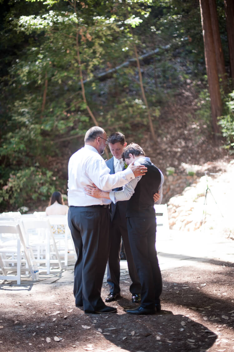 Three men in a circle holding each other with their heads bowed