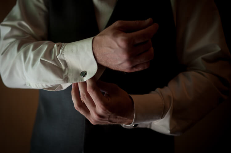 A man putting on cufflinks on his long-sleeved shirt