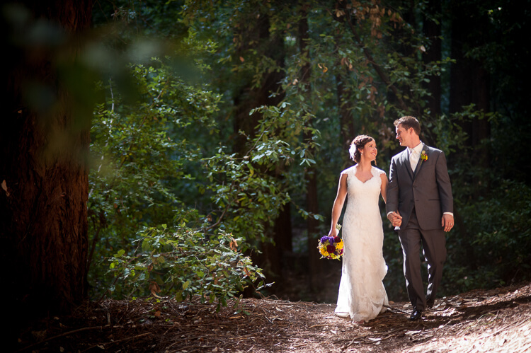 A bride and groom walking on a trail in the woods