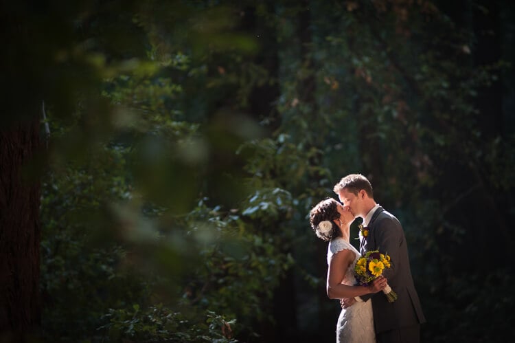 A groom kissing his bride in front of trees