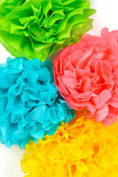 A close up of four paper cut flowers, in blue, green, yellow and pink