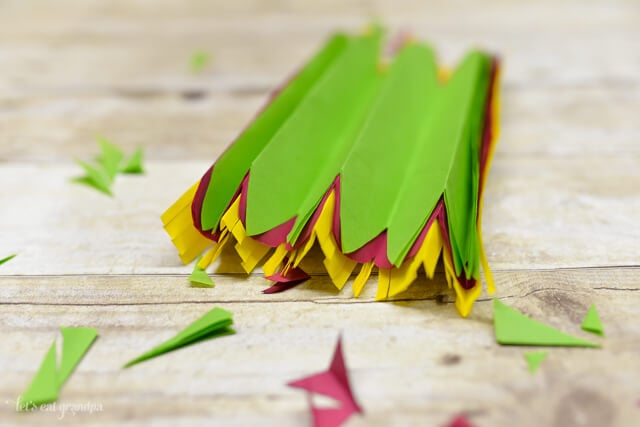 magenta, yellow, and green tissue paper sheet stacked and folded accordion on wooden background with edges cut off