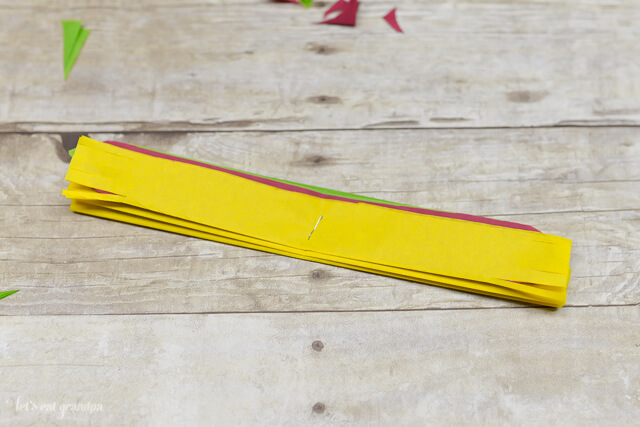 magenta, yellow, and green tissue paper strips cut and stacked on wooden background