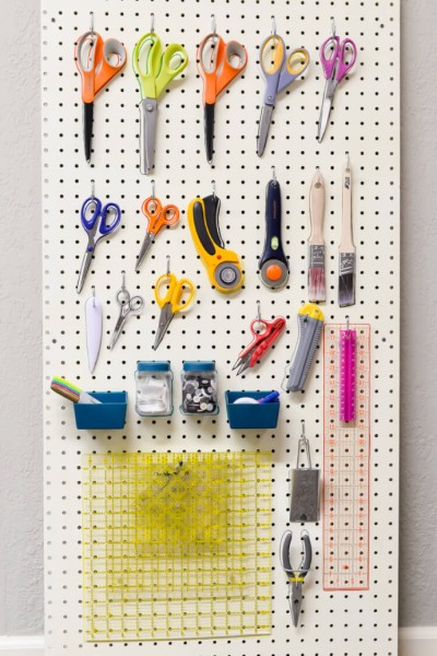 A pegboard filled with craft supplies such as scissors, paint brushes, rulers and rotary cutters