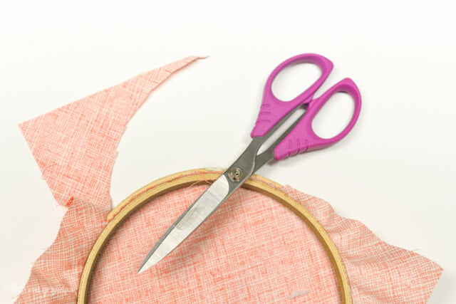 scissors cutting orange fabric to fit embroidery hoop