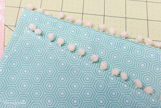 Fabric with pom poms attached to it lying on top of a green mat