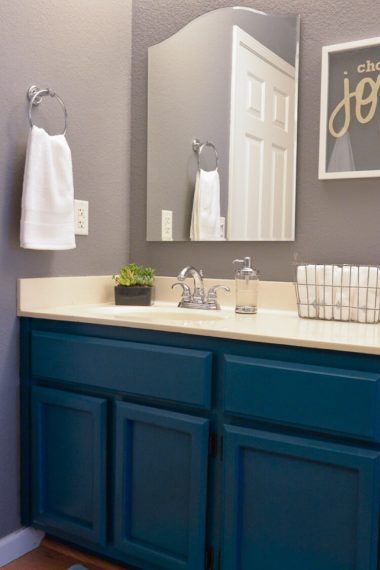 This makeover of a 1980s oak bathroom is stunning! Dark teal cabinets, modern lighting, and fun details make this bathroom makeover a showstopper.