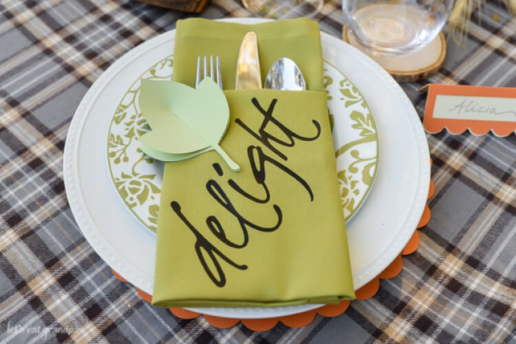 A place setting with two plates and a napkin folded into a pocket holding a fork, knife and spoon