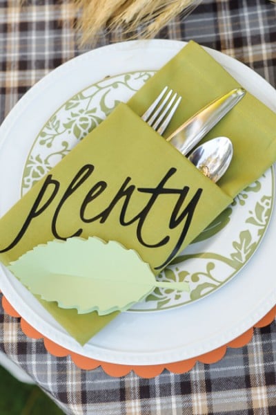 A place setting with two plates and a napkin folded into a pocket holding a fork, knife and spoon