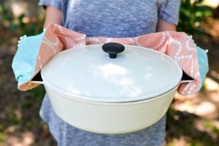 A woman holding a huge pan using a potholder