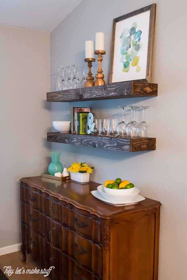wooden floating shelves in kitchen with glasses and home decor and kitchen buffet below shelves