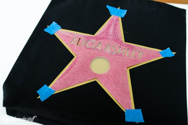 Image of a gold star with a pink personalized star taped over the top of it against a black background 