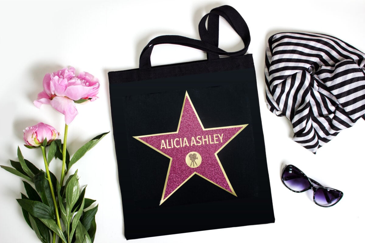 Two peony flowers, a pair of sunglasses, a black and white striped scarf and a black tote bag decorated with a star and personalized with a name