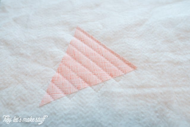 A close up of a triangular piece of fabric quilted to a piece of batting