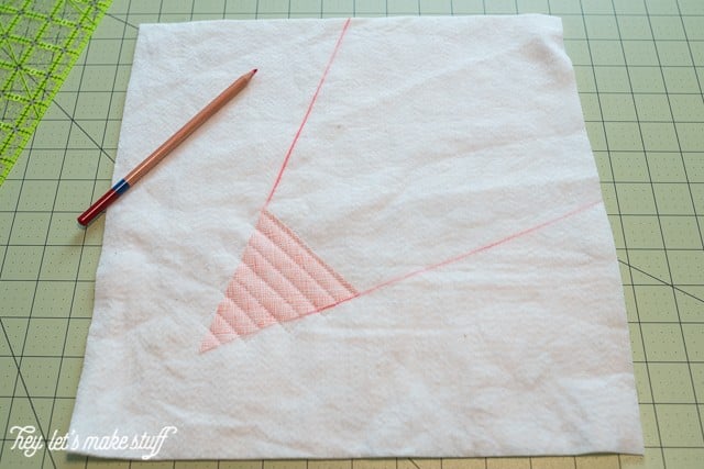 A triangular piece of fabric quilted to a piece of batting, a pencil and a ruler all on top of a mat