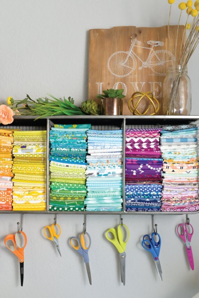 A shelf filled with fabric and scissors hanging on hooks below the shelf