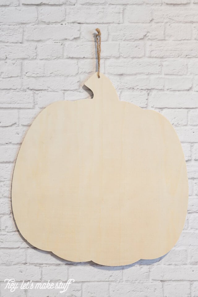 wooden pumpkin cutout hung on white brick wall