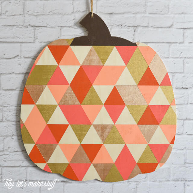 finished geometric painted pumpkin hanging on white brick fireplace