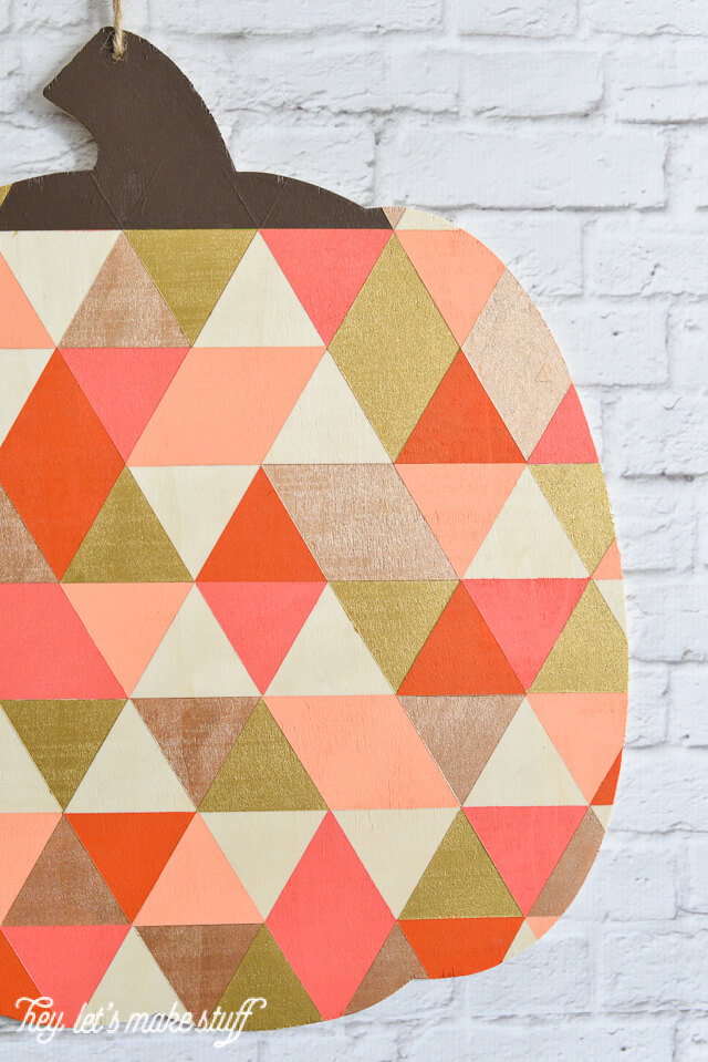 side view of finished geometric painted pumpkin hanging on white brick fireplace