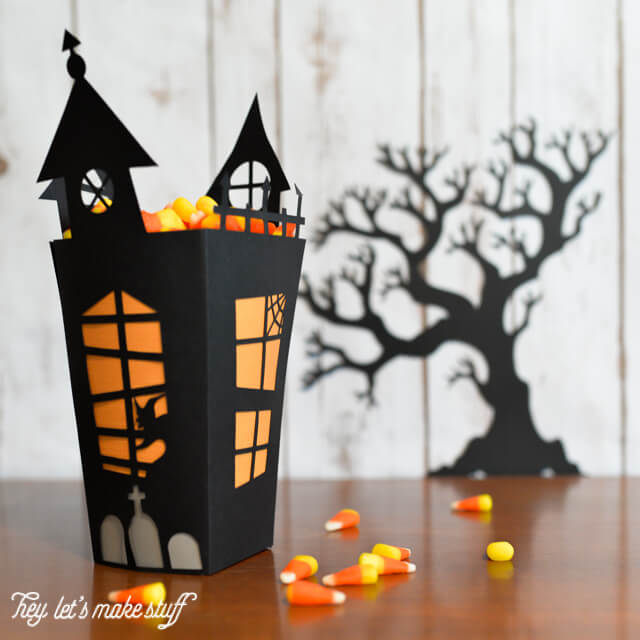 A black box that resembles a haunted house filled with candy corn and a silhouette of a black scary tree in the background