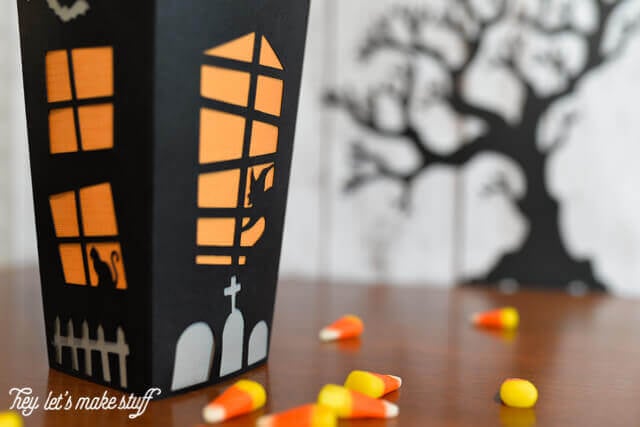 Close up of a black box that resembles a haunted house filled with candy corn and a silhouette of a black scary tree in the background