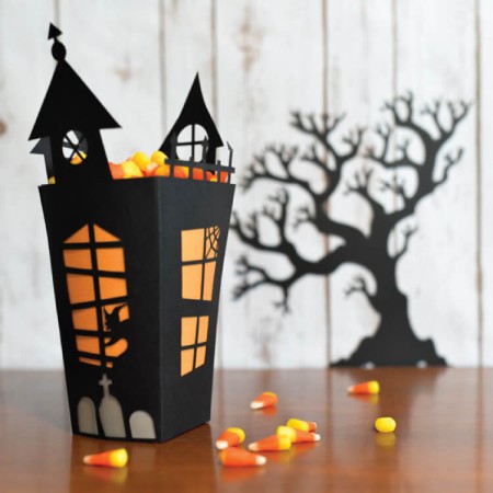 A black box that resembles a haunted house filled with candy corn and a silhouette of a black scary tree in the background