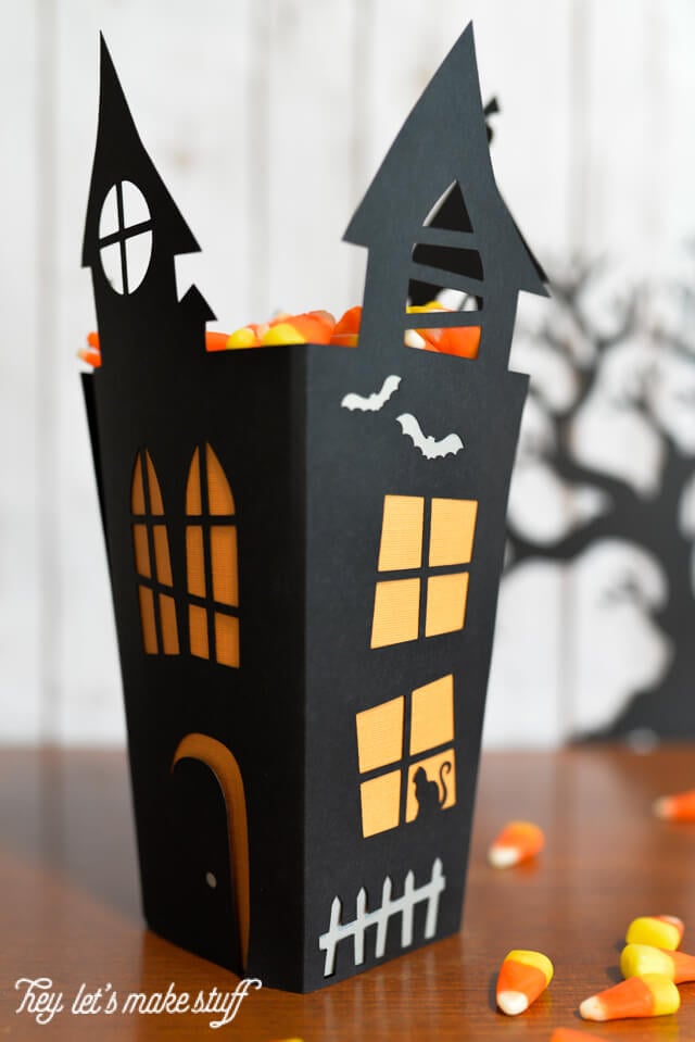 Close up of a black box that resembles a haunted house filled with candy corn and a silhouette of a black scary tree in the background