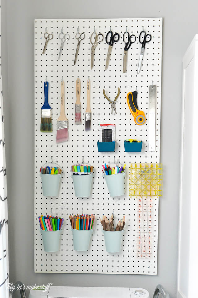 A pegboard hanging on a wall, filled with crafting tools, paint brushes, scissors, markers and more