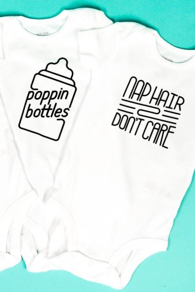 Two white onesies against an aqua blue background and one is decorated with a baby bottle that says, "Poppin Bottles" and the other one says, "Nap Hair Don't Care"
