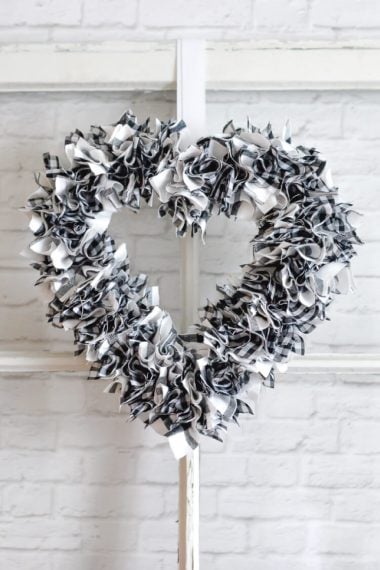 A black and white fabric wreath hanging on a window that is leaned up against a white brick wall