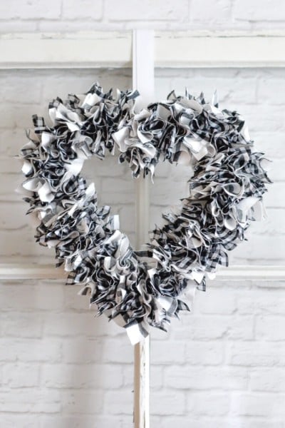 A black and white fabric wreath hanging on a window that is leaned up against a white brick wall