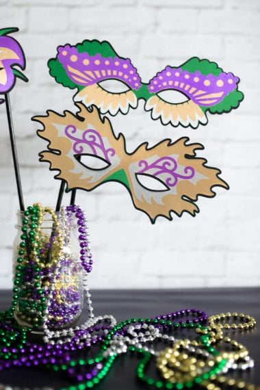 Mardi Gras masks and beads sitting in and hanging out of a jar that is sitting on a table