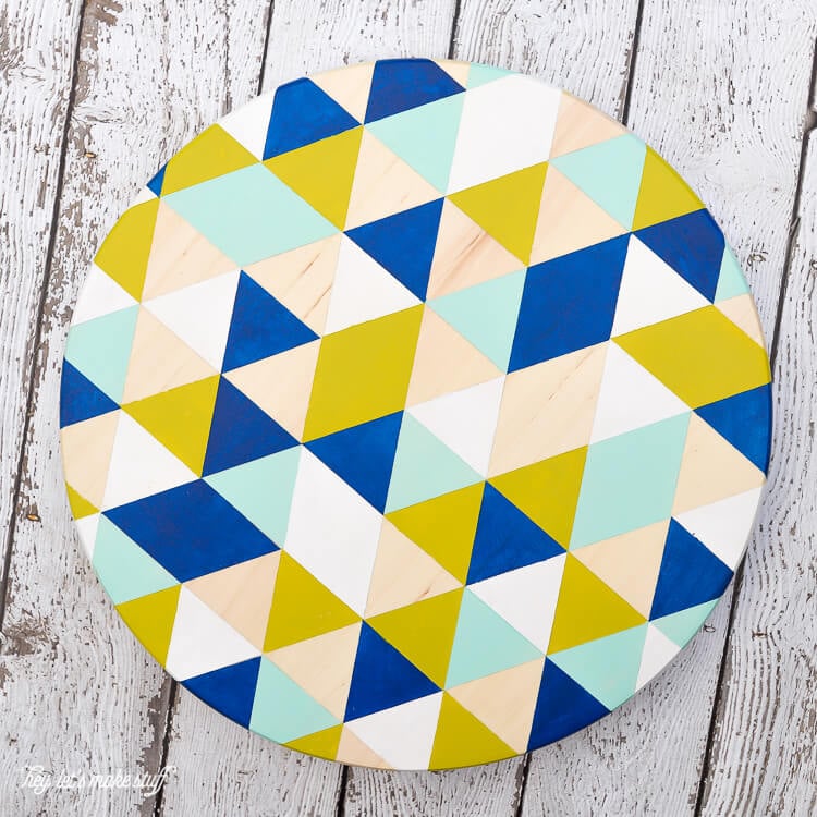 A round piece of wood painted with a geometric design, sitting on a wooden table