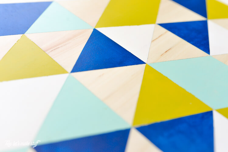 A round piece of wood with white, yellow, light blue, dark blue and peach painted triangles and diamonds