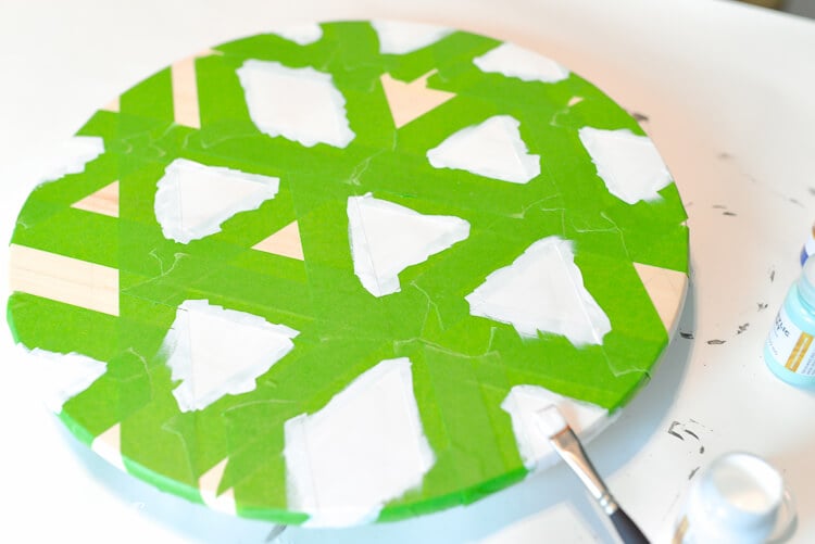 A round piece of wood with green tape all over it with white painted triangles and diamonds