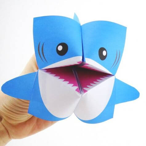 A hand holding a finger puppet that is shaped like a shark
